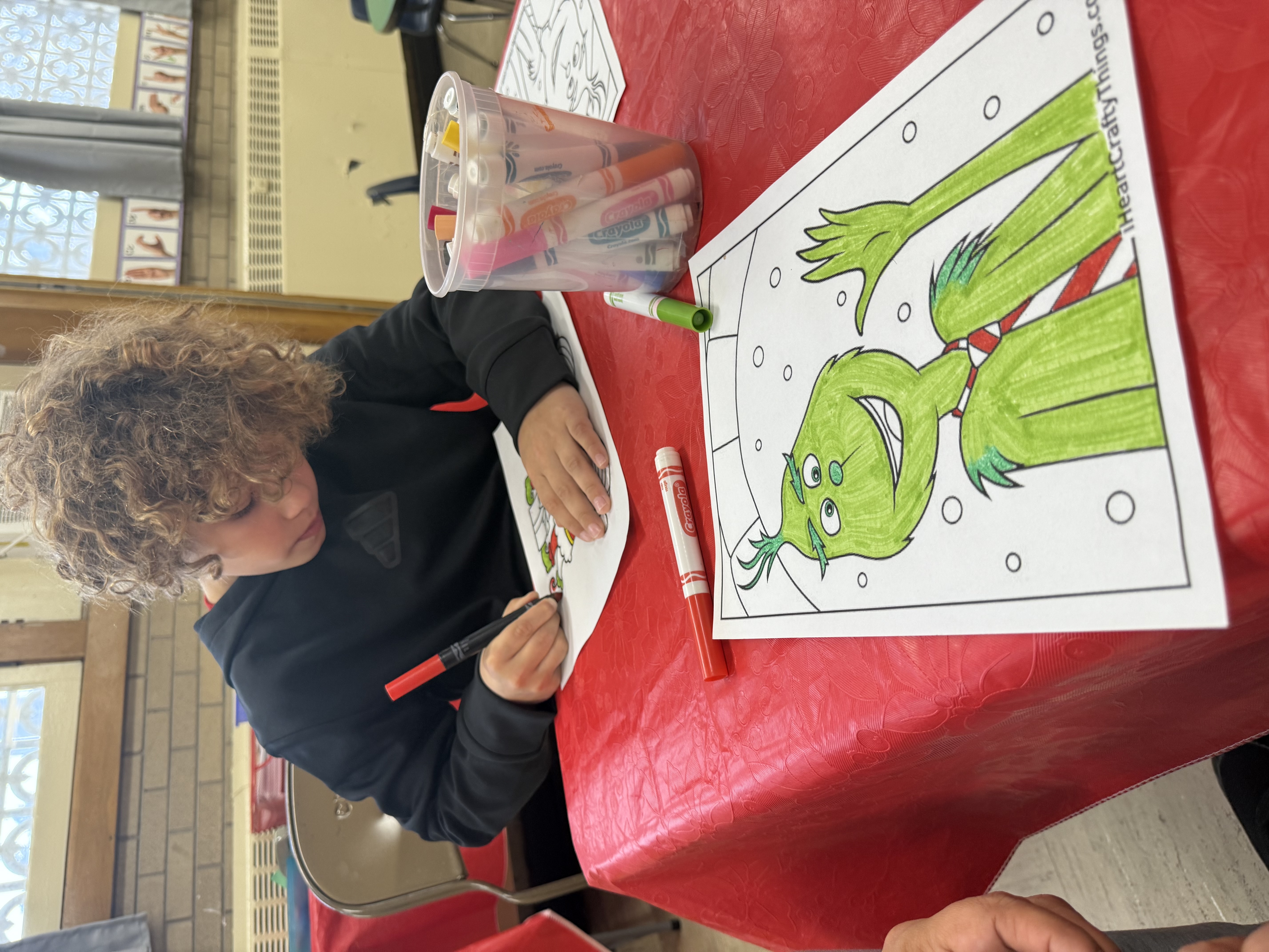 Child coloring Grinch graphic with markers.